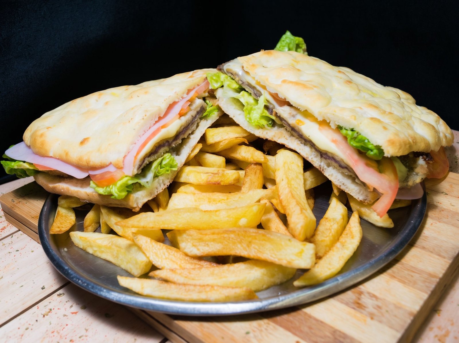 Sánguche de milanesa en pan de pizza con jamón, queso y lechuga, acompañado de papas fritas